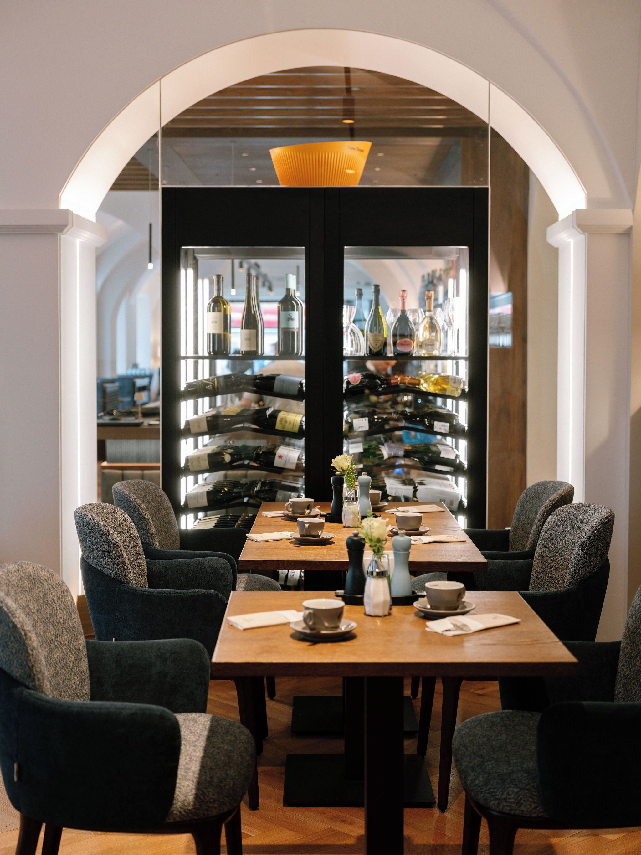 A dining area with a long table, chairs, and a wine rack in the background.