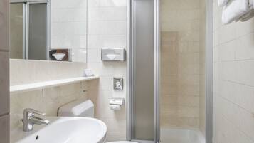 Un baño moderno con lavamanos blanco, inodoro y cabina de ducha con paredes de cristal.