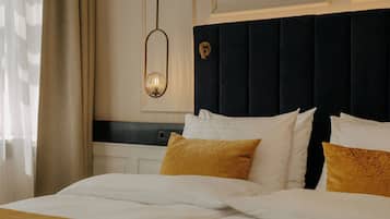 A neatly made bed with white and gold bedding, a dark headboard, and a wall-mounted light fixture.