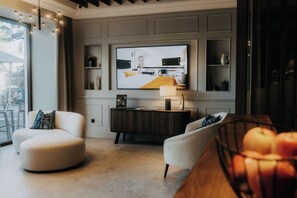 A modern living room with a large flat-screen TV, a round white sofa, a smaller armchair, and a wooden coffee table. - IMLAUER Palais Mirabell (Salzburg)
