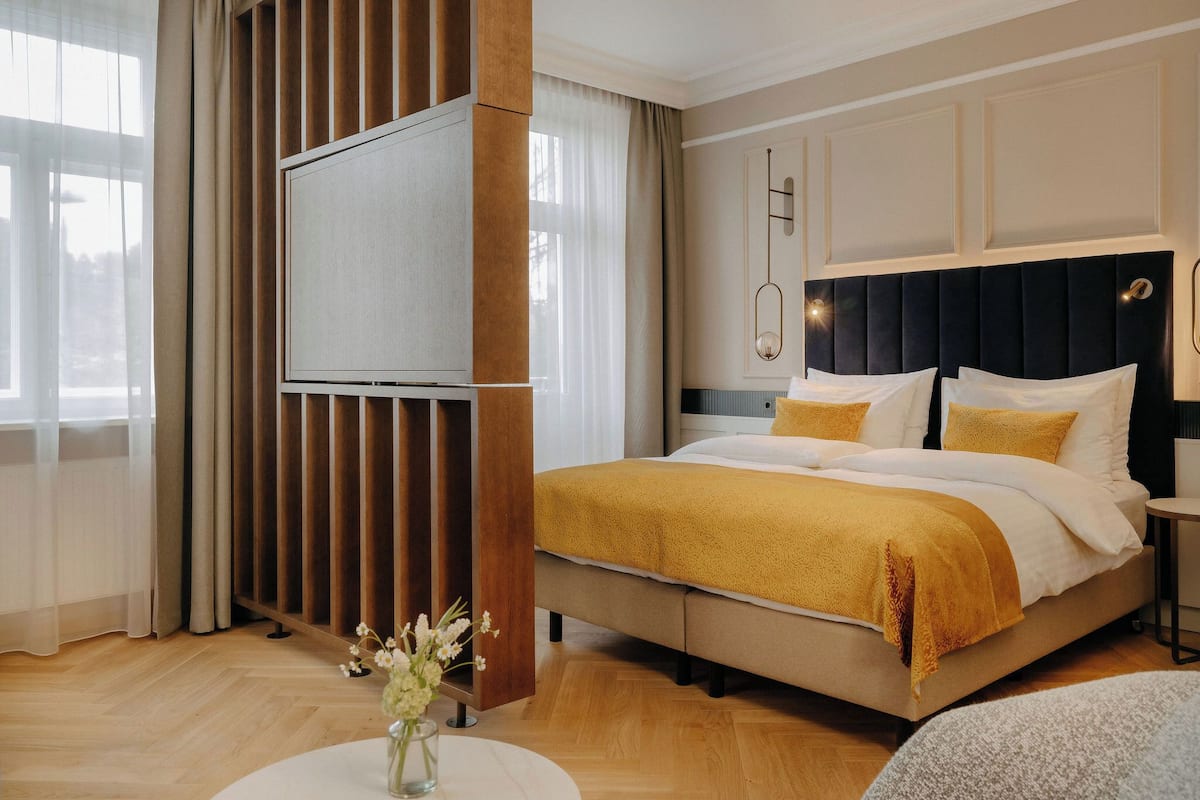 Habitación de hotel con cama, televisión, un jarrón con flores y vistas al exterior.
