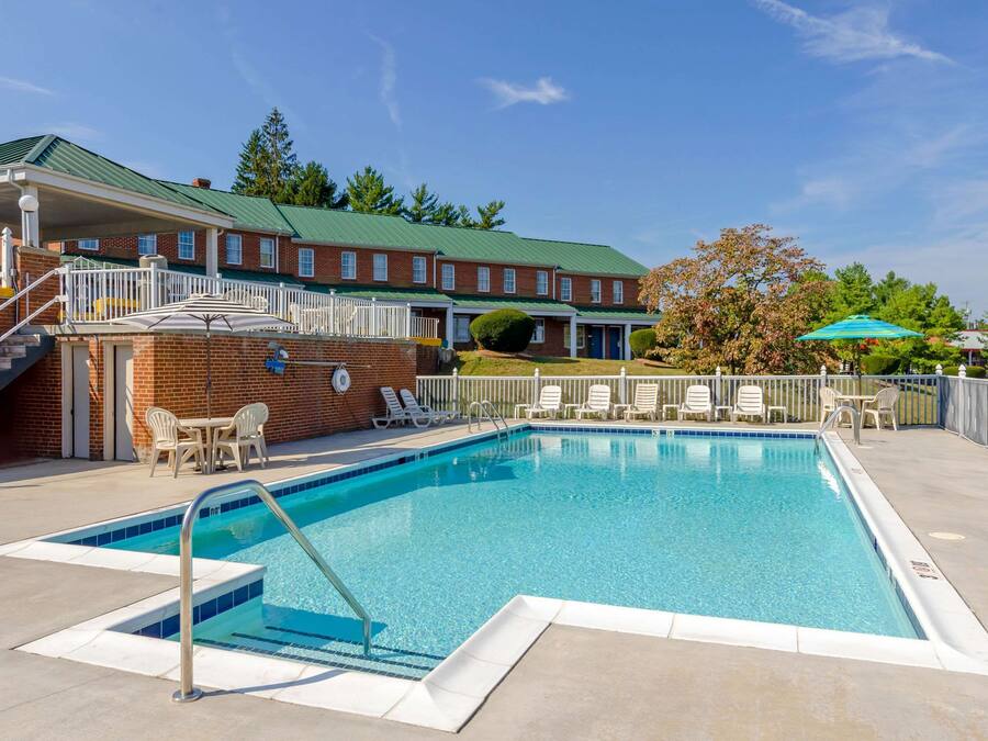 A rectangular swimming pool with a metal ladder, surrounded by a white deck. There are lounge chairs and a covered seating area with a green roof.