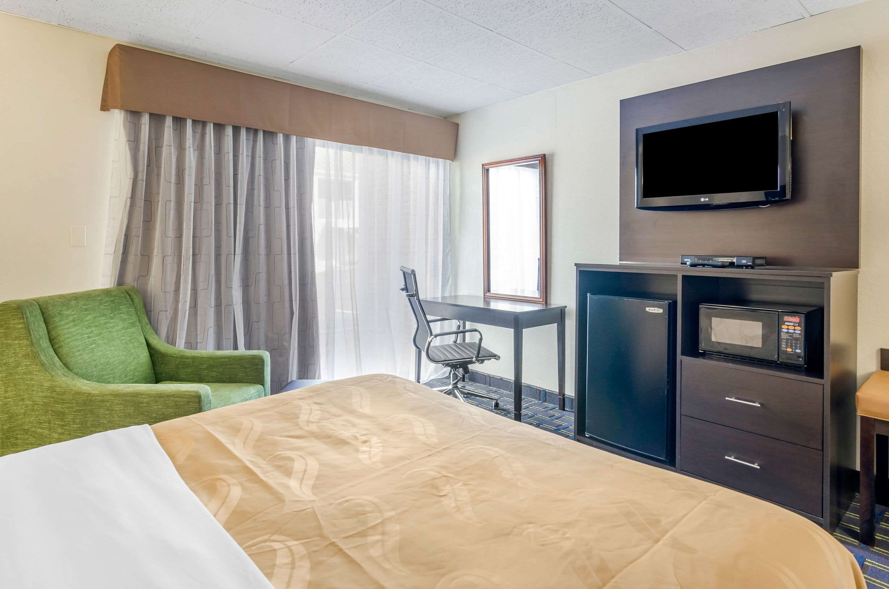 Een hotelkamer met een bed, een bureau, een stoel, een televisie, een magnetron en een minibar.