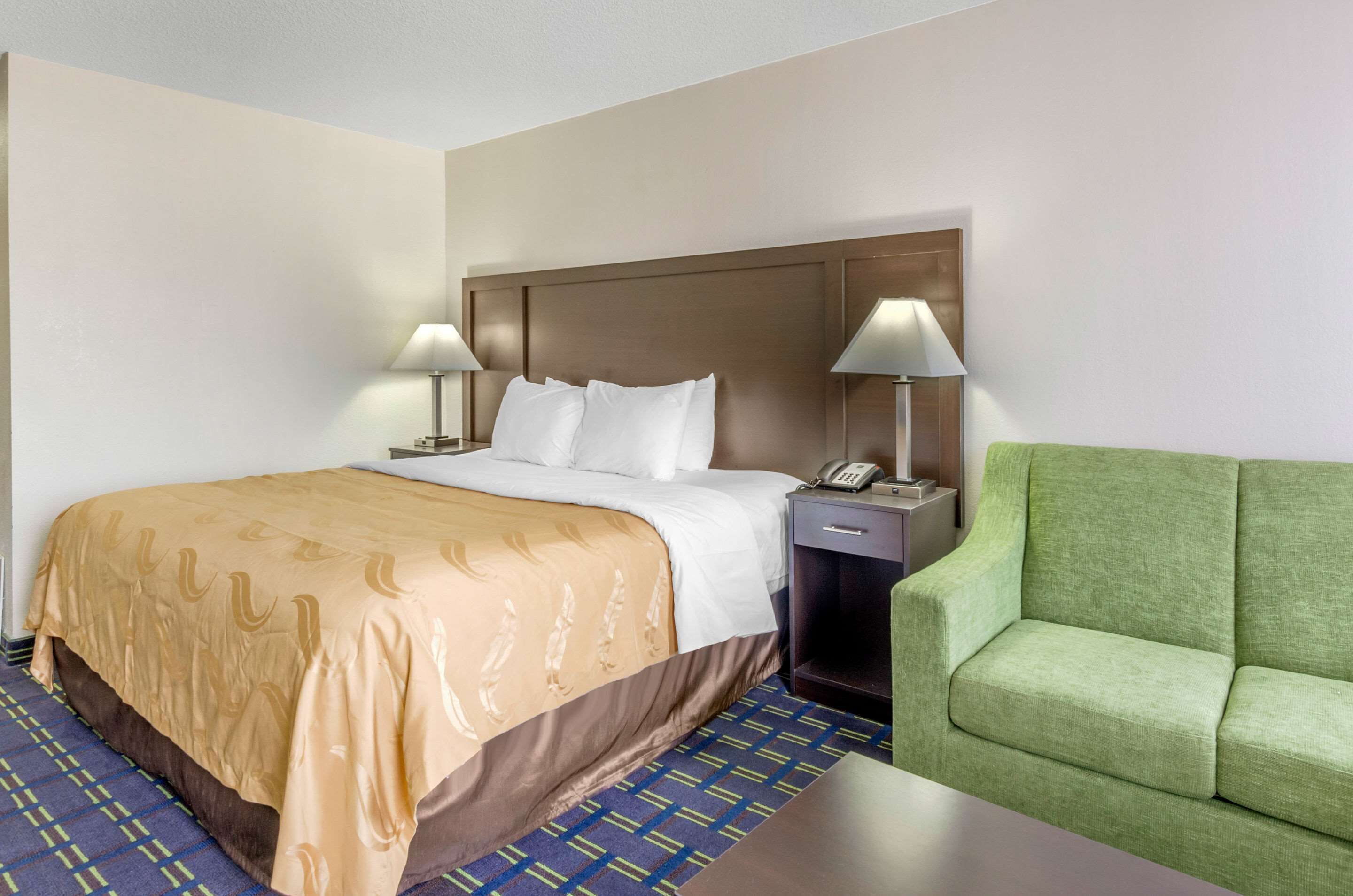 A hotel room with a large bed, two bedside lamps, a green sofa, and a small table.