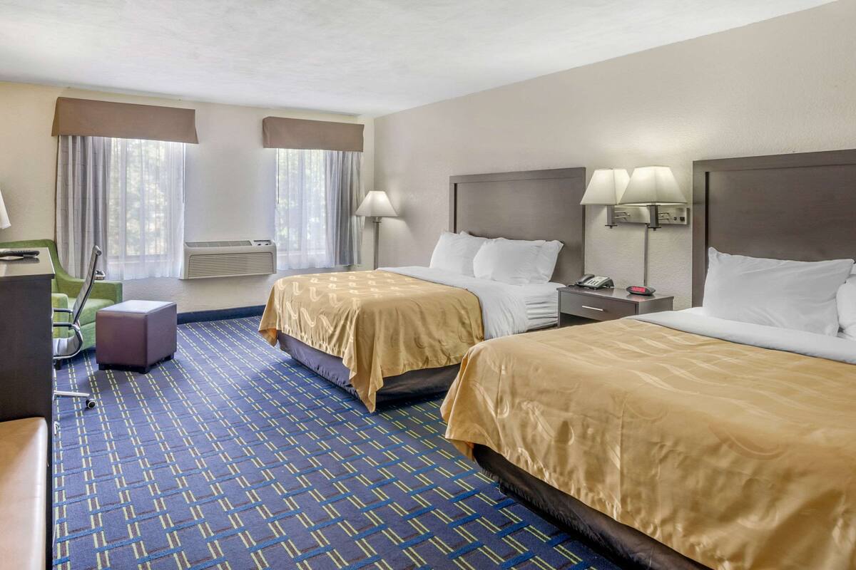 A hotel room with two beds, a desk, a chair, and a window with curtains.