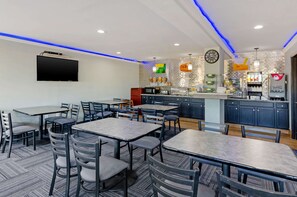 A modern restaurant with tables and chairs, a kitchen area, and a flat-screen TV mounted on the wall.