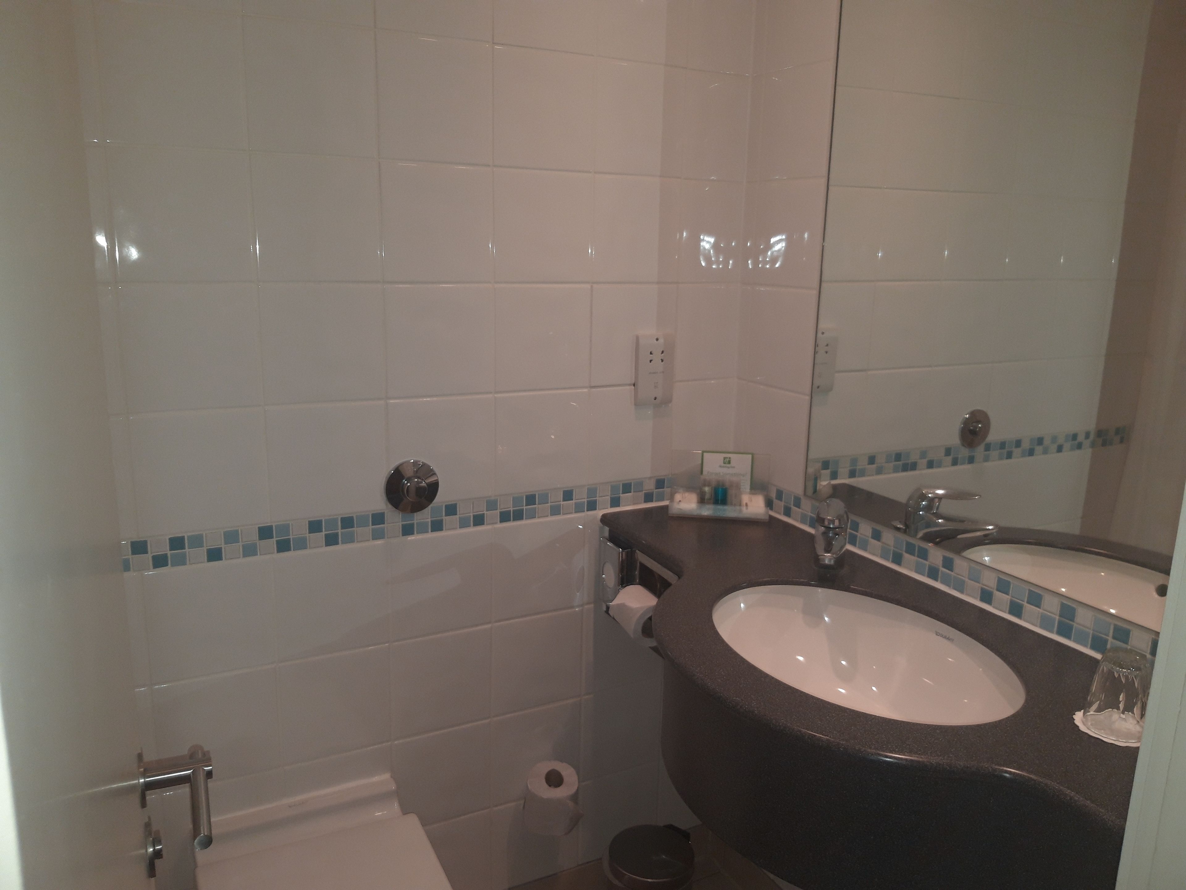 A bathroom with white tiled walls, a black sink, a mirror, and a toilet.
