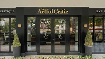 L’entrée du restaurant The Artful Critic se distingue par sa façade noire, ses portes vitrées et les deux plantes en pot qui l’encadrent de chaque côté.