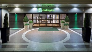 L’extérieur d’un hôtel Holiday Inn, doté d’un design moderne, avec une entrée illuminée de lumière verte et une allée circulaire.