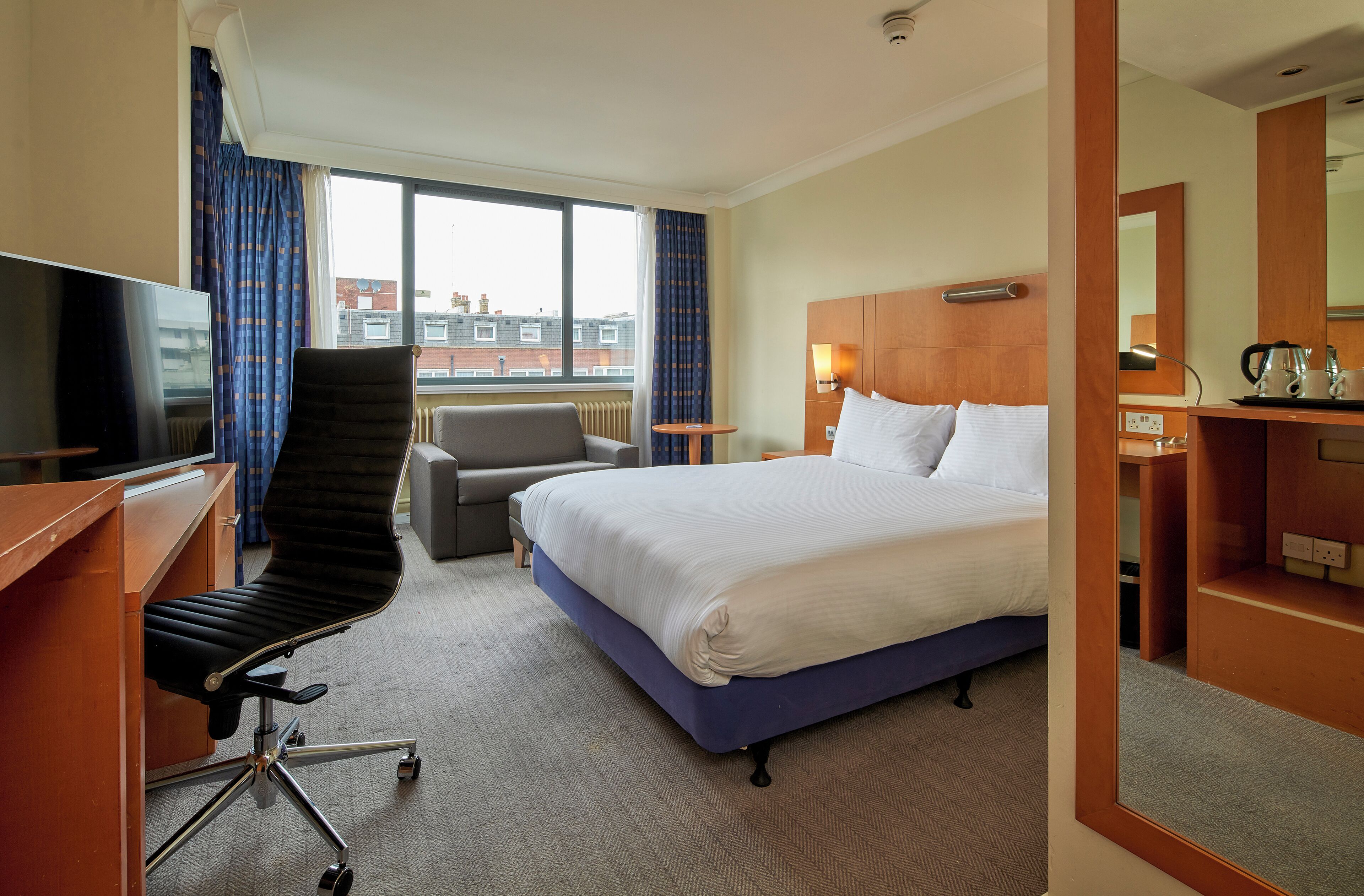 Une chambre d’hôtel équipée d’un lit, d’un bureau, d’une chaise, d’une télévision et d’une fenêtre avec des rideaux.