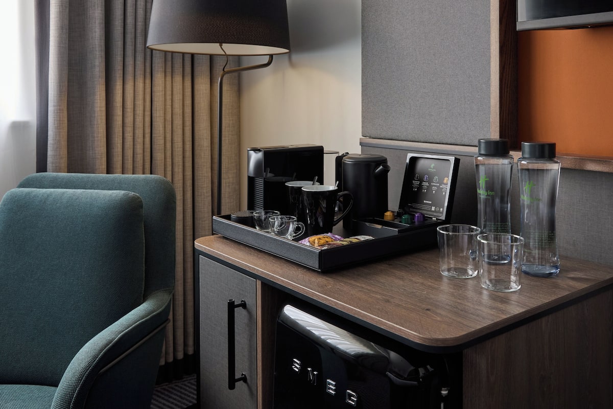 A hotel room with a kitchenette, a coffee maker, a tea kettle, and two water bottles on the counter.