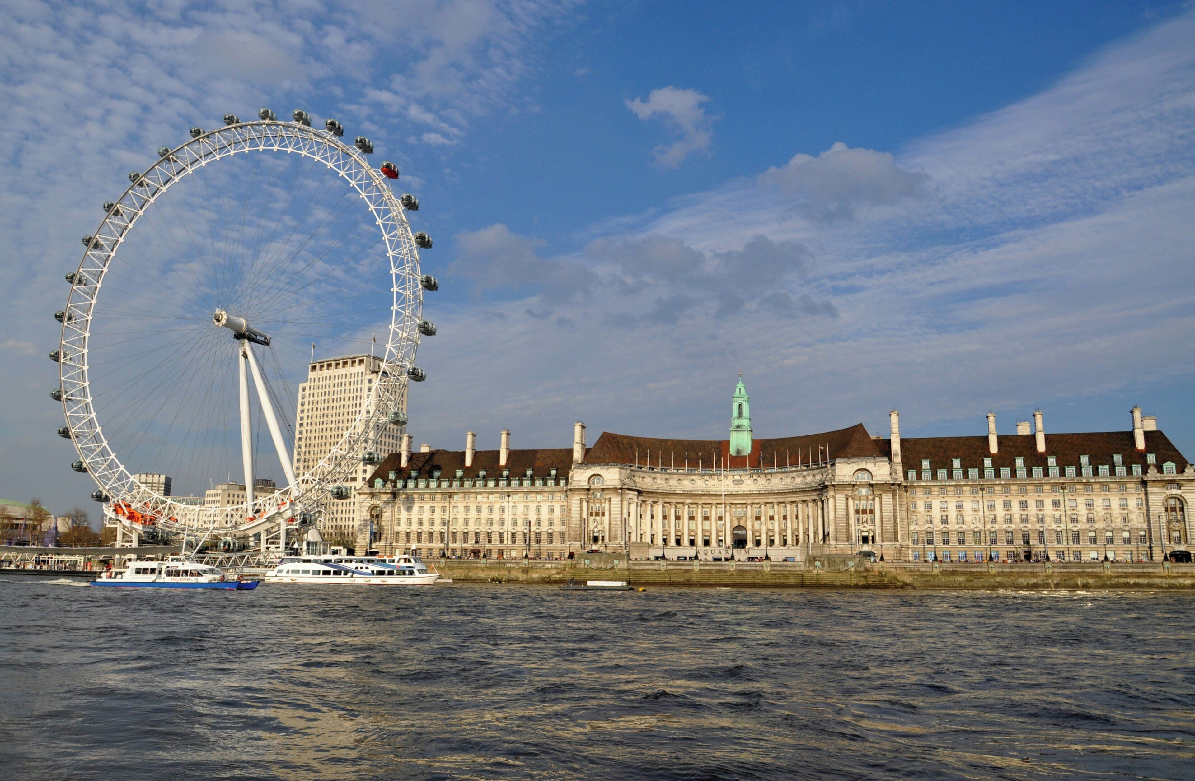 A large Ferris wheel and a historic building with a clock tower across a body of water.