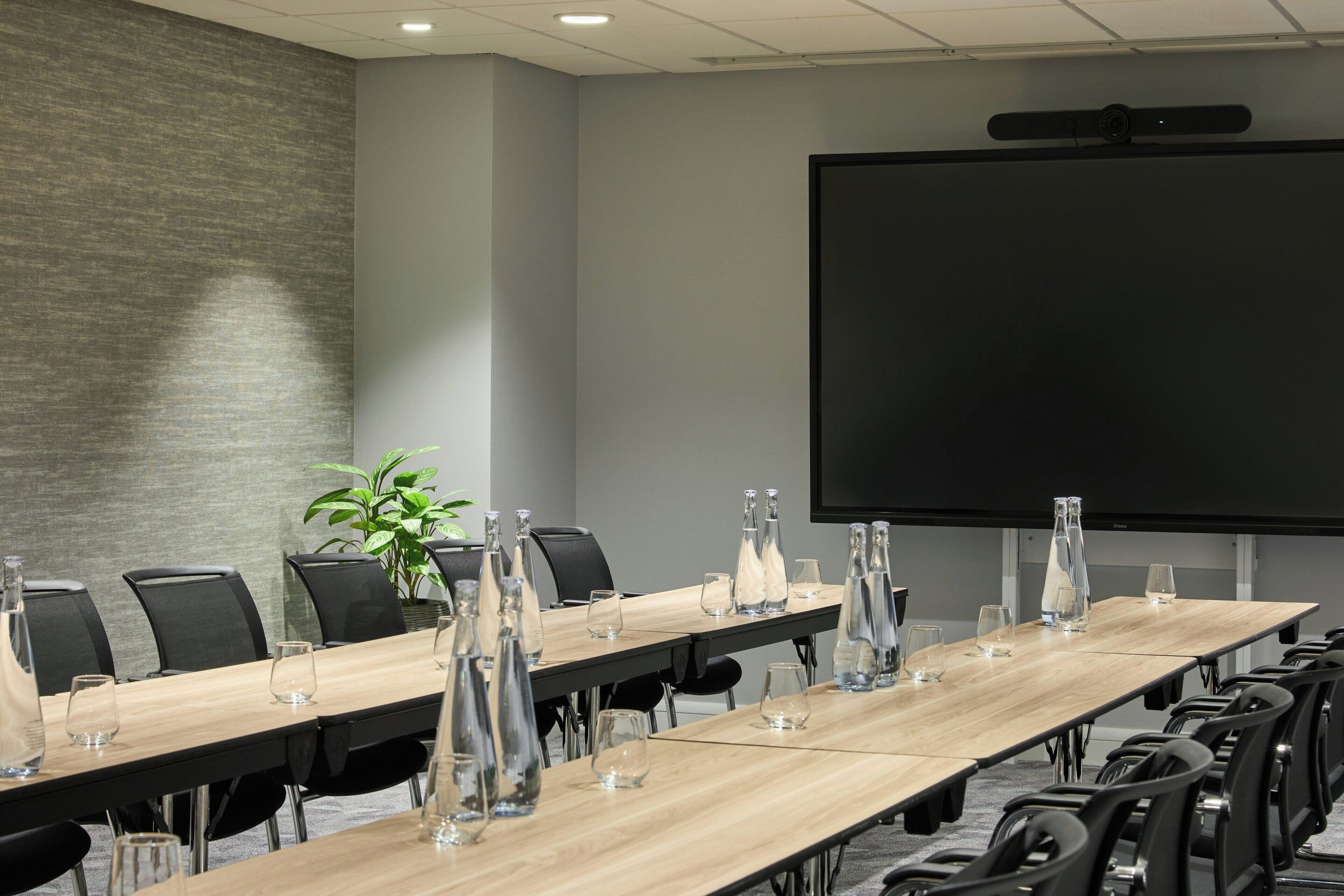 A conference room with a long table, chairs, a projector screen, and glassware.