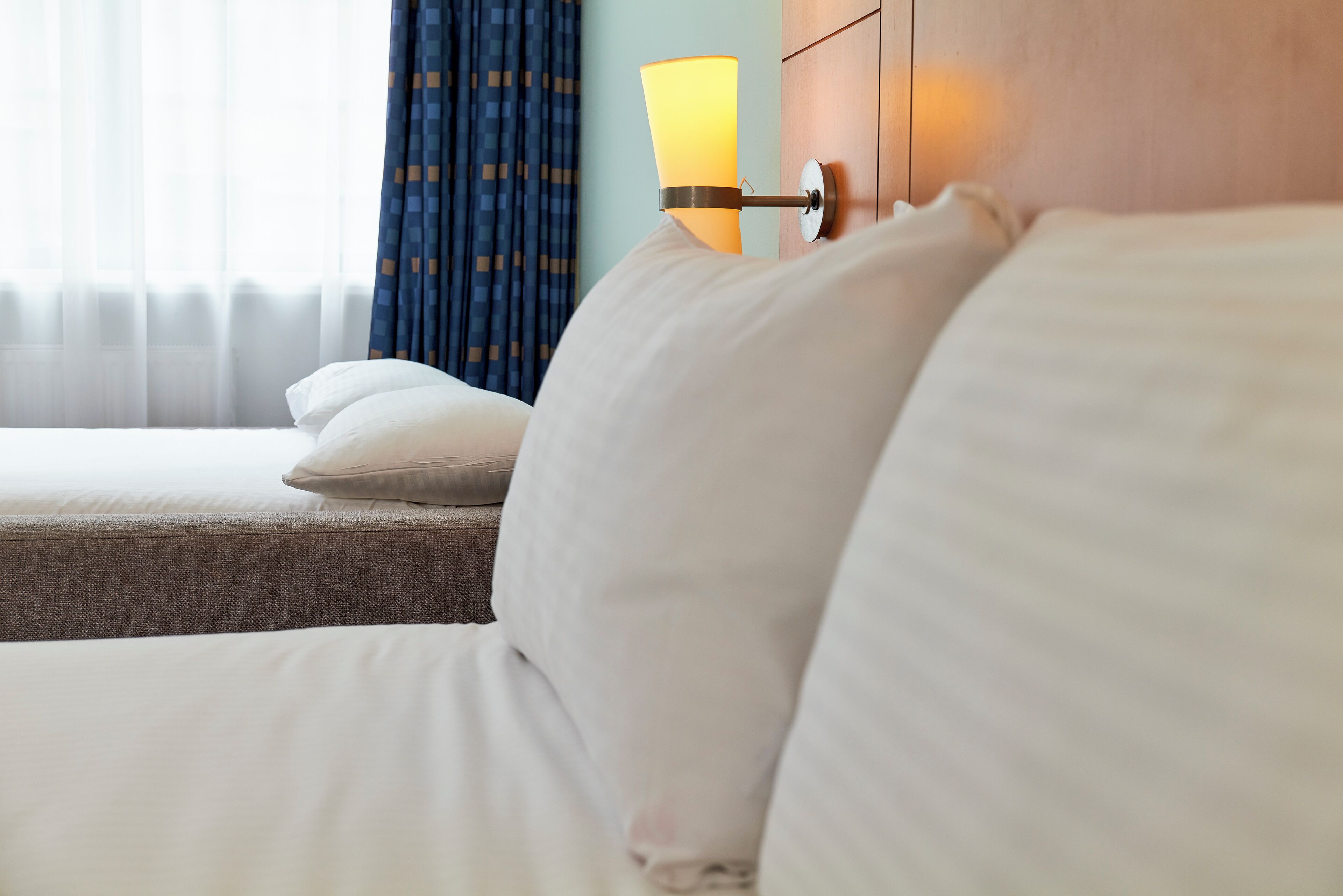 A hotel room with a bed, a nightstand, a lamp, and a window with curtains.