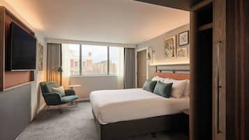 Une chambre d’hôtel avec un grand lit, une chaise, une petite table et un téléviseur fixé au mur.