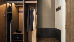 Un dressing avec des vêtements suspendus, un porte-chaussures et une petite étagère sur laquelle se trouve une télécommande.