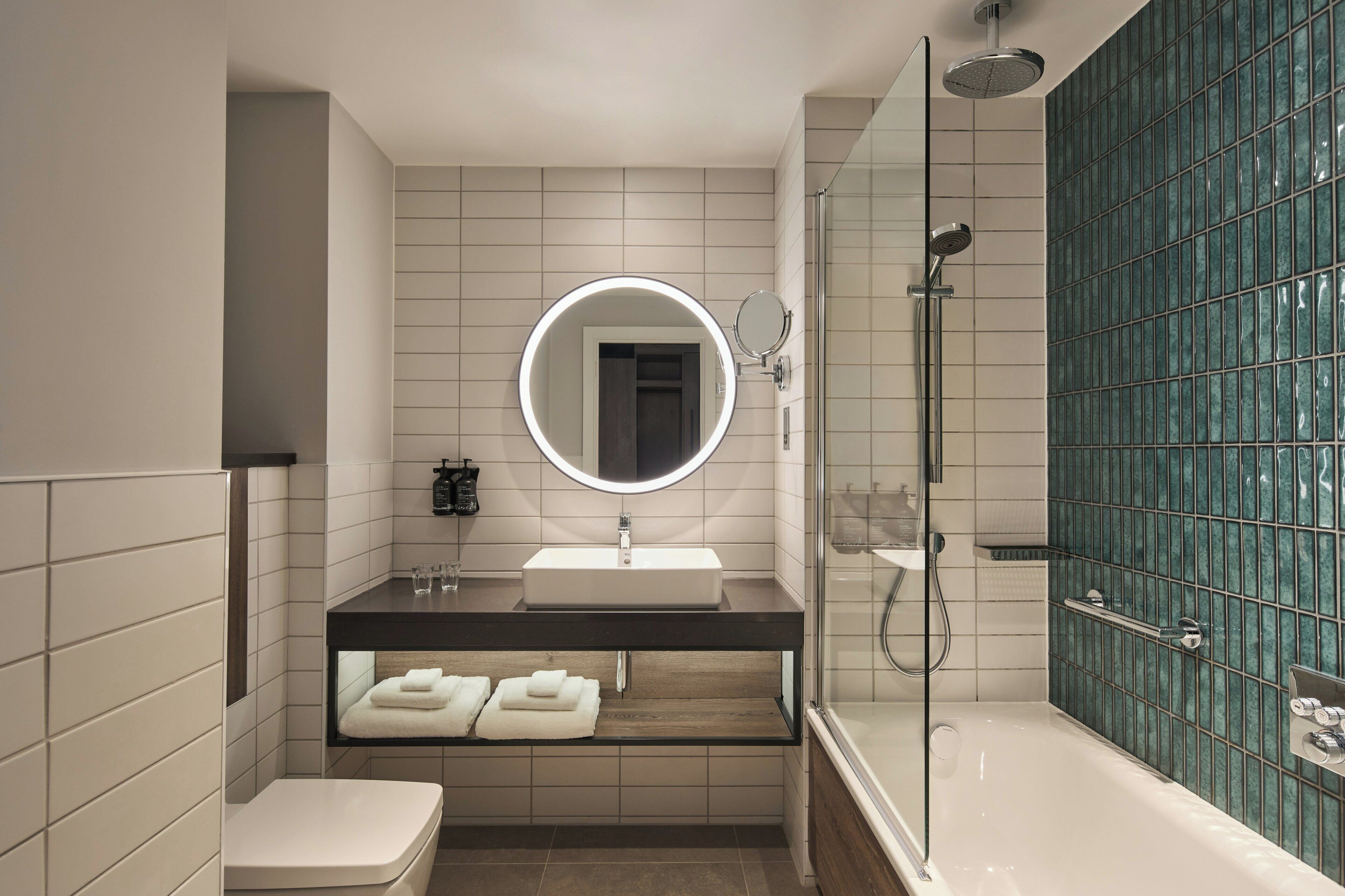 Une salle de bain moderne avec une douche à parois de verre, un lavabo blanc et un miroir doté d’un cadre circulaire.