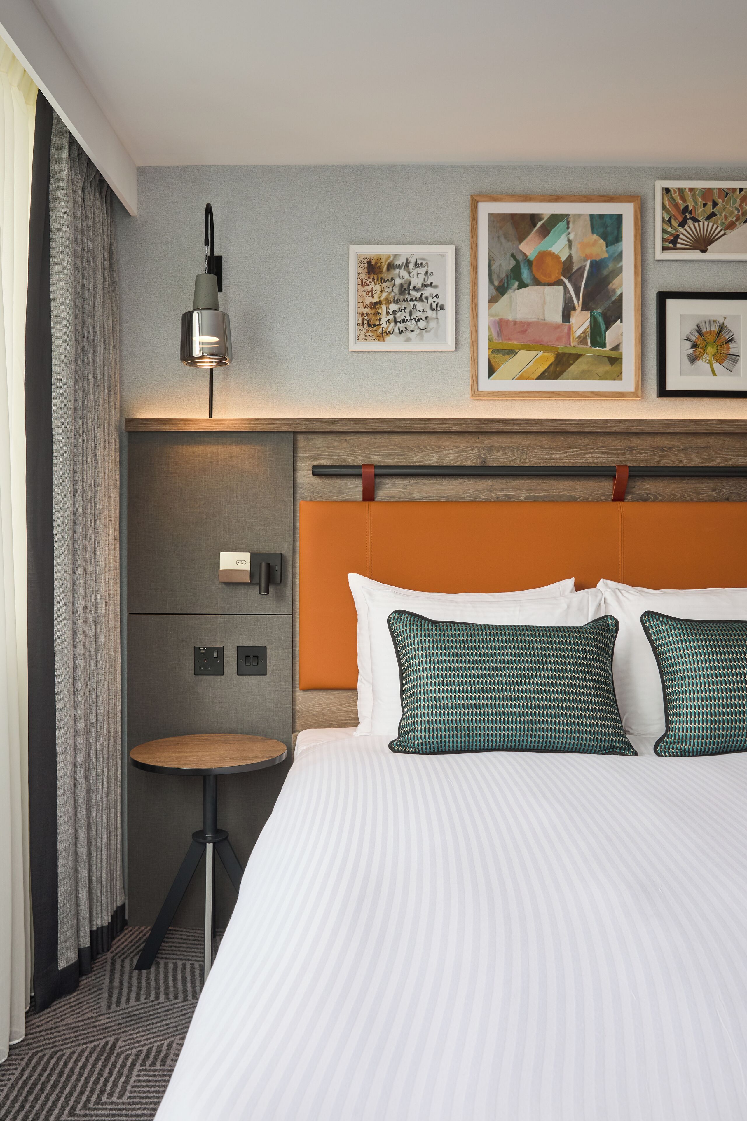 A hotel room with a large bed, a bedside table, a lamp, and artwork on the wall.