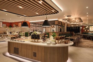 A modern restaurant with a central island, multiple seating areas, and a variety of lighting fixtures.