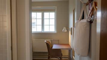 Un pasillo que conduce a una habitación con suelo de madera, un radiador, una ventana y un escritorio con una silla.