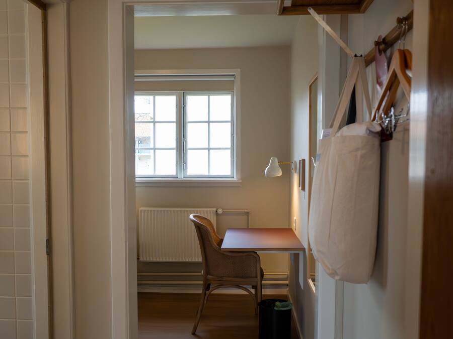 Un pasillo que conduce a una habitación con suelo de madera, un radiador, una ventana y un escritorio con una silla.
