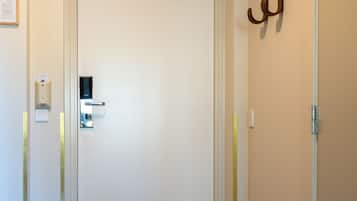 A hotel entrance with a white door, a doormat, a wall-mounted coat hook, and a wall-mounted light switch.