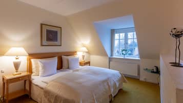 A neatly arranged bedroom with a large bed, two bedside tables with lamps, a framed picture on the wall, a window with a view, and a radiator.