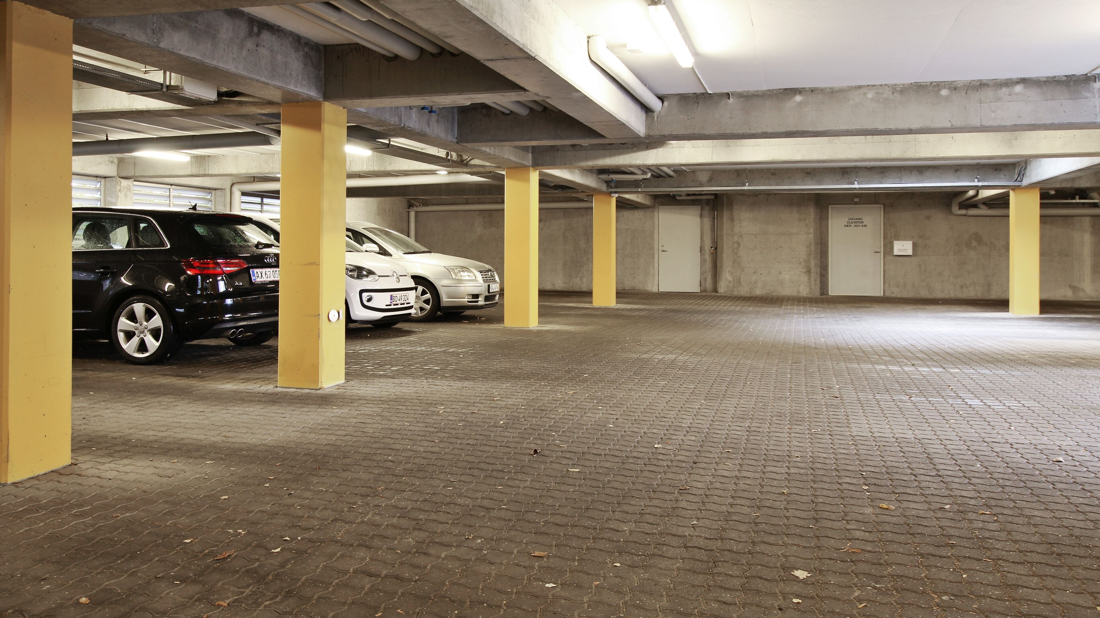 An underground parking garage with two cars parked, concrete pillars, and a tiled floor.