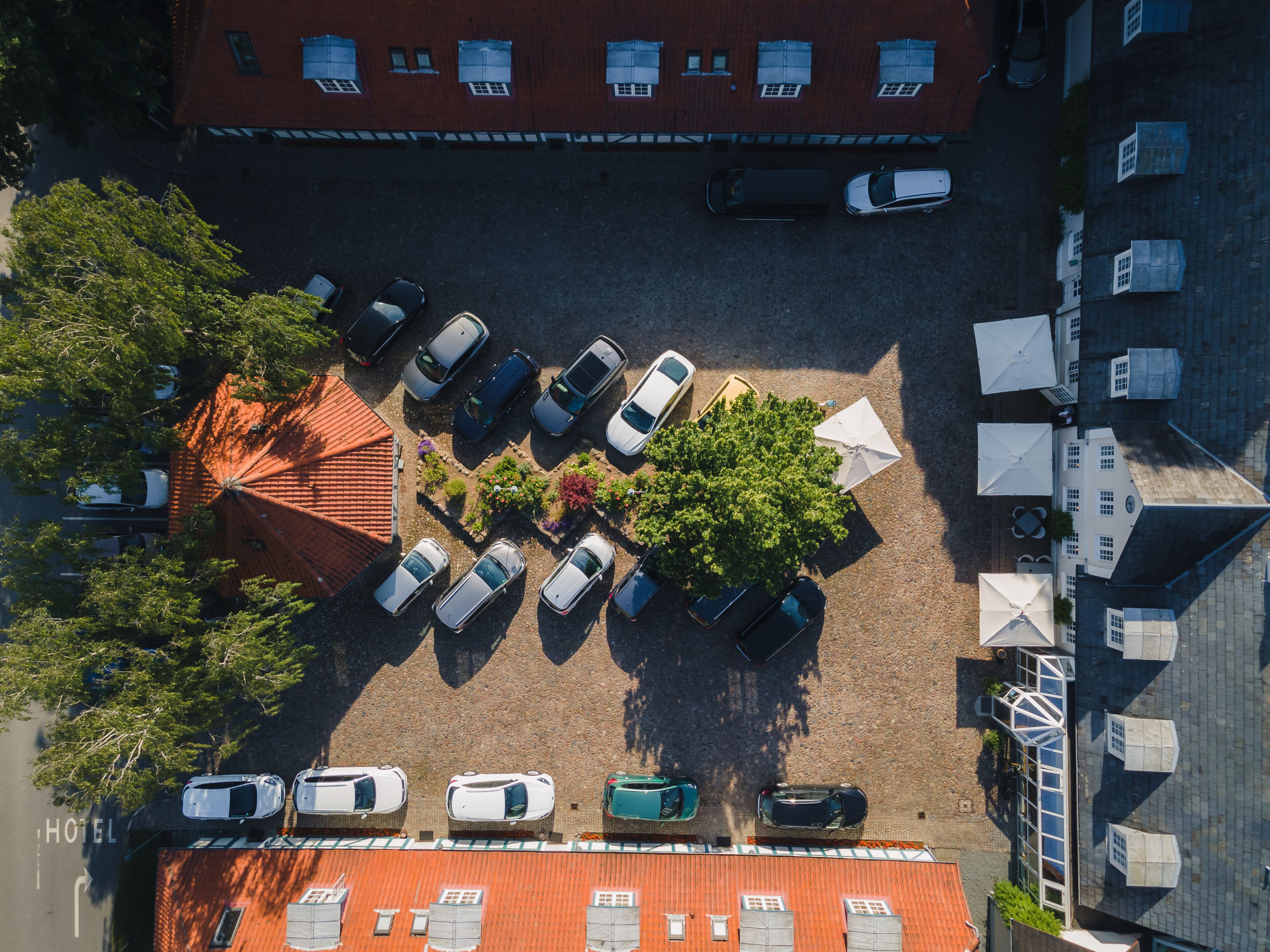 An aerial view of a parking lot with multiple cars, a hotel building, and a tree.