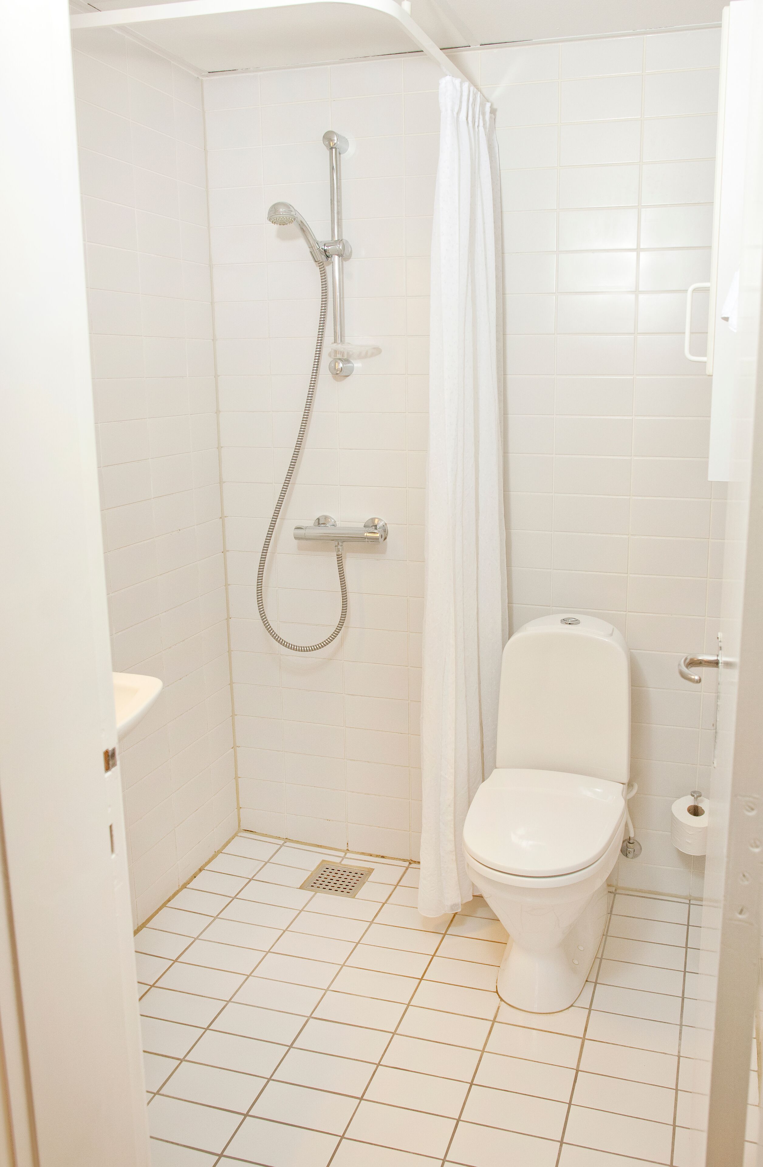 A small, white bathroom with a shower, toilet, and a white curtain.