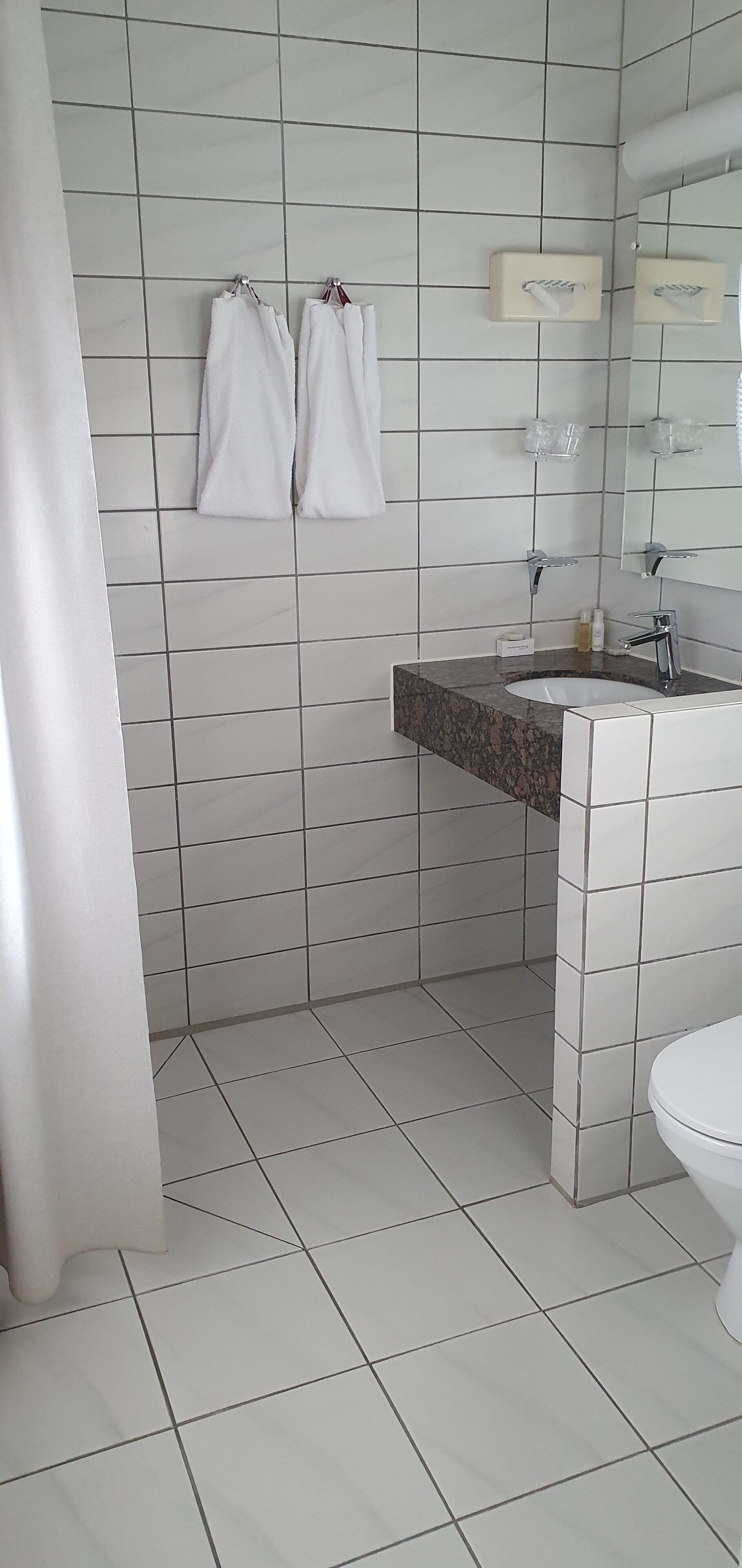 A bathroom with white tiled walls, a granite countertop sink, and a white toilet.
