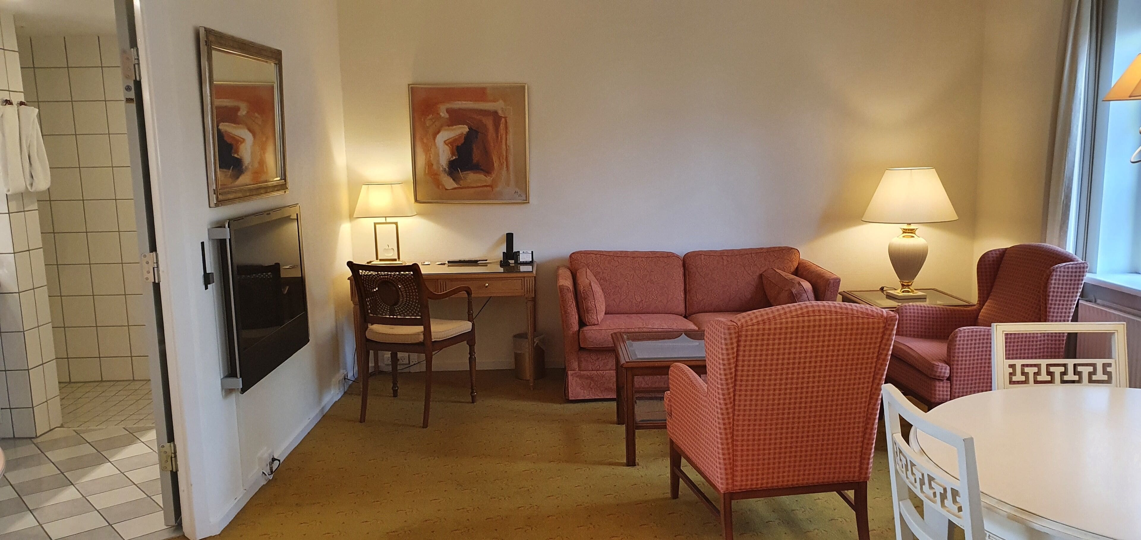 Un salon comprenant un canapé, des fauteuils, une table, un téléviseur et des œuvres d’art accrochées aux murs.