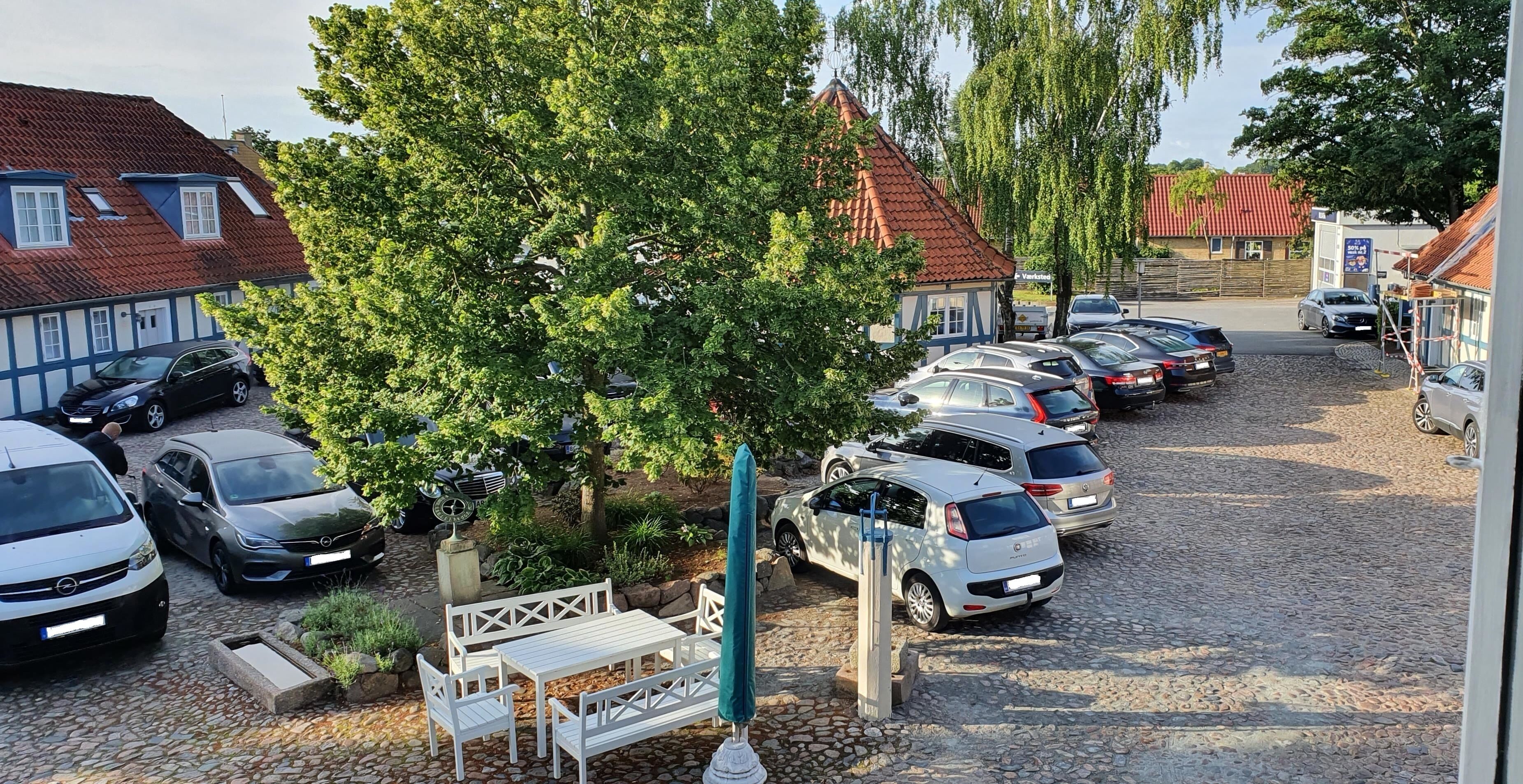 A parking area with several cars, a small outdoor seating area, and a building with a red-tiled roof.