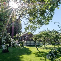 A traditional house with a sloped roof, surrounded by a well-maintained lawn and flowering trees.