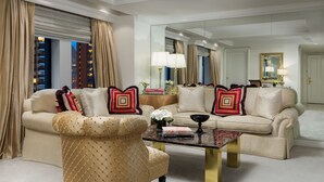 A luxurious living room with a beige sofa, a matching armchair, and a coffee table. There is a large mirror on the wall and a window with curtains.