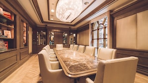A spacious conference room with a marble table and leather chairs, a chandelier, and a view through a large window.
