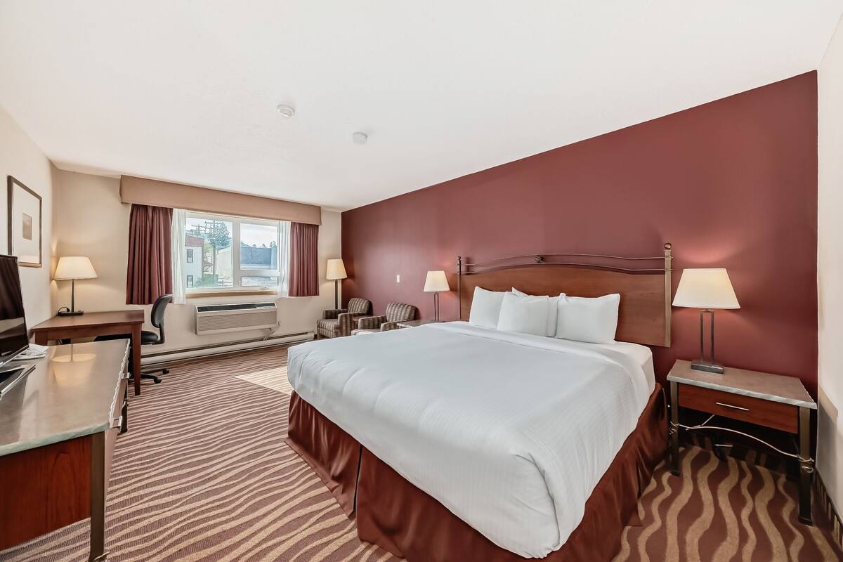 Ein Hotelzimmer mit einem großen Bett, einem Schreibtisch, einem Stuhl, einem Fernseher und einem Fenster mit Vorhängen.