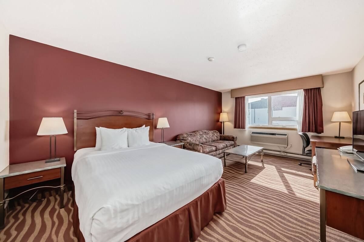Ein Hotelzimmer mit einem großen Bett, einer Couch, einem Schreibtisch und einem Fenster mit Vorhängen.