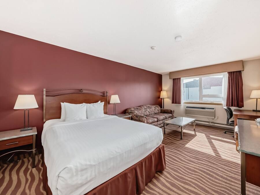 Una habitación de hotel con una cama grande, un sofá, un escritorio y un ventanal con cortinas.