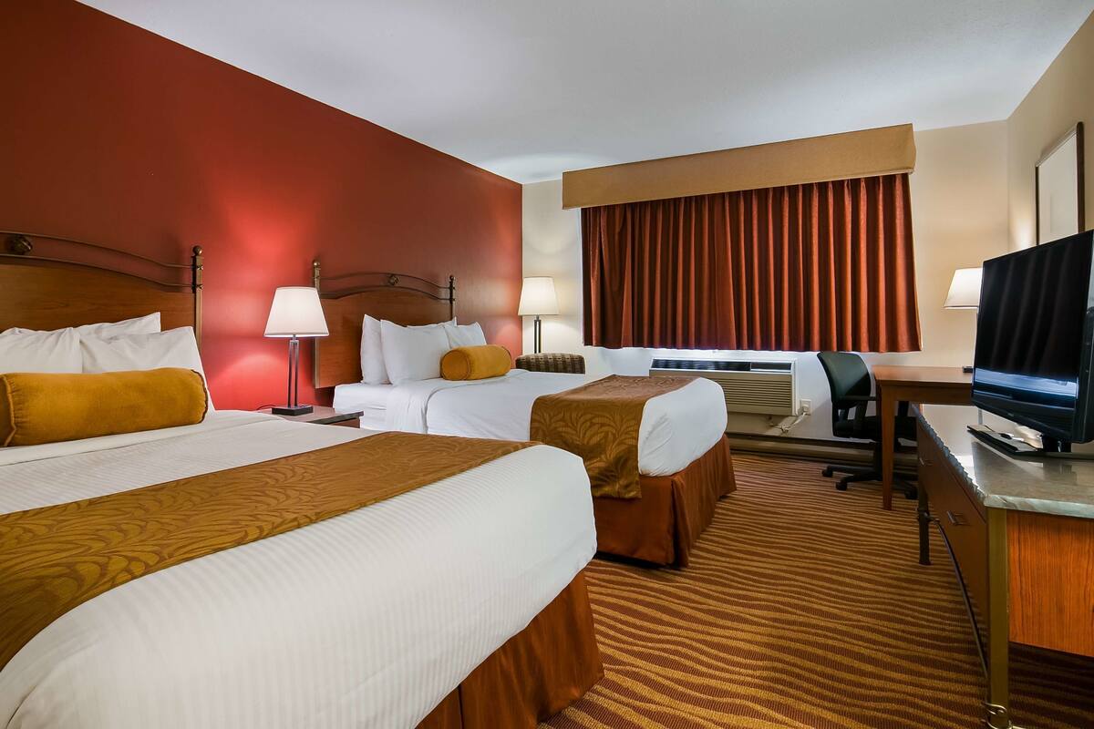 Ein Hotelzimmer mit zwei Betten, einem Schreibtisch, einem Fernseher und einem fenster mit Vorhängen.