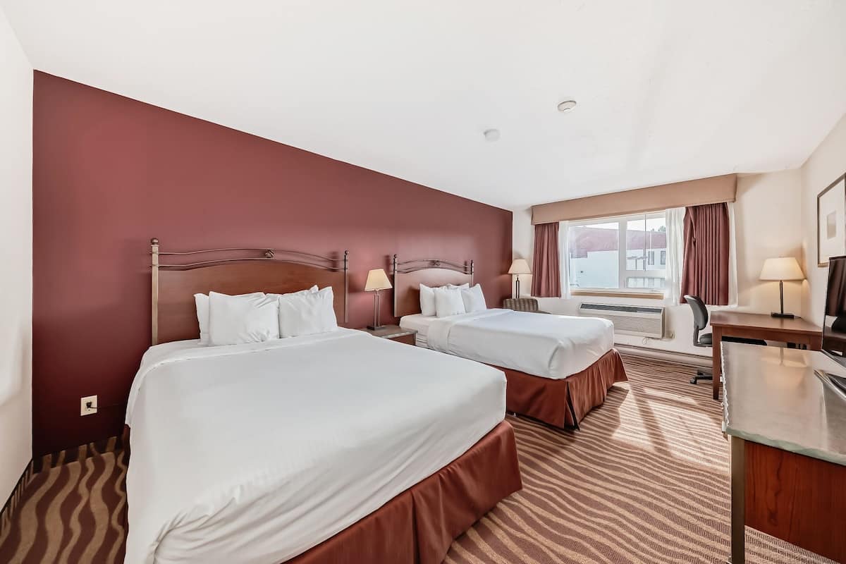 Ein Hotelzimmer mit zwei Betten, einem Schreibtisch und einem Fenster mit Vorhängen.