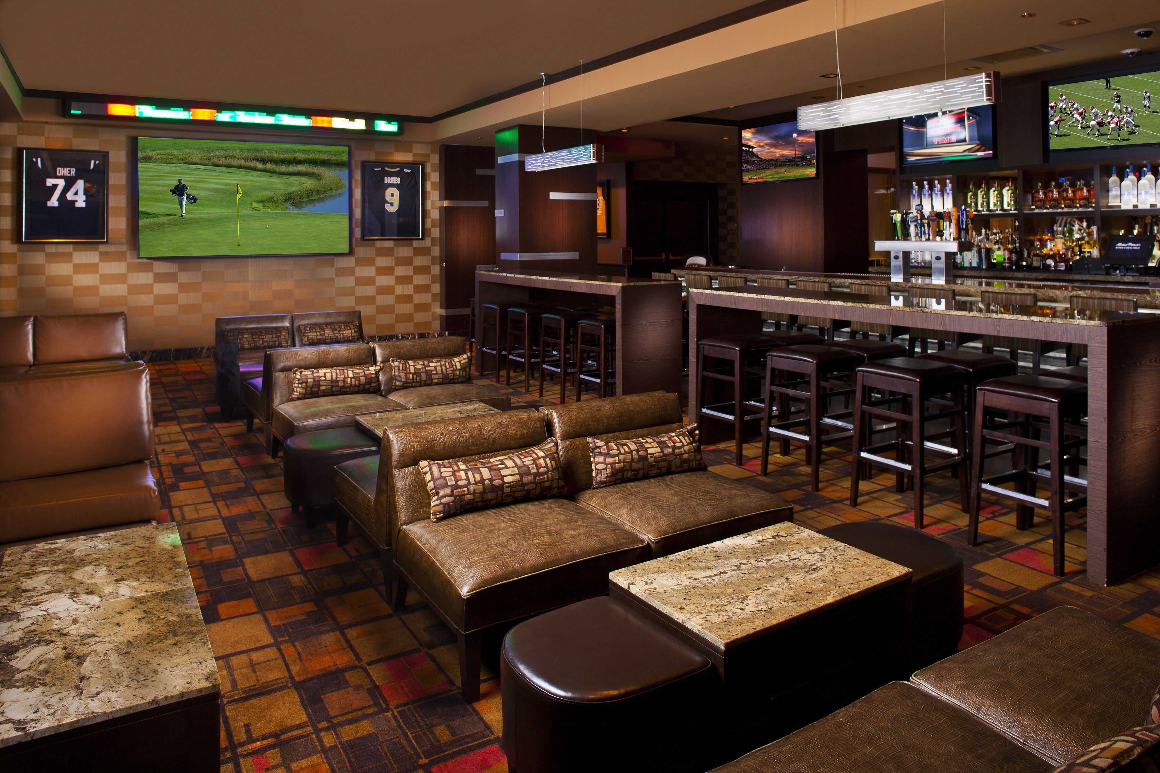 A bar area with leather seating, a bar counter, and a television screen displaying sports.