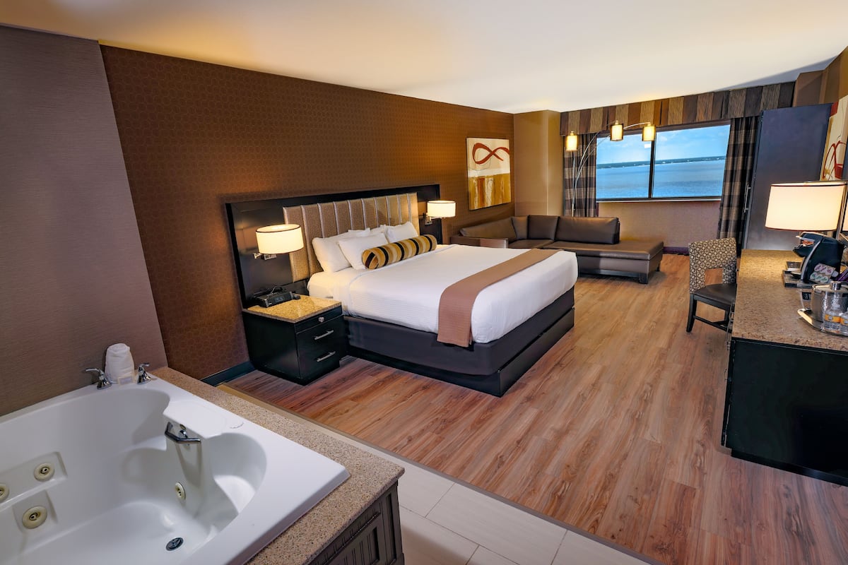 A hotel room with a large bed, a sitting area, a desk, and a view of the sea.