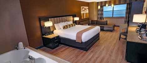 A hotel room with a large bed, a sitting area, a desk, and a view of the sea.