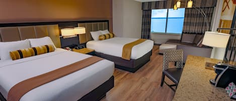 A hotel room with two beds, a desk, a chair, a lamp, and a view of the sea.