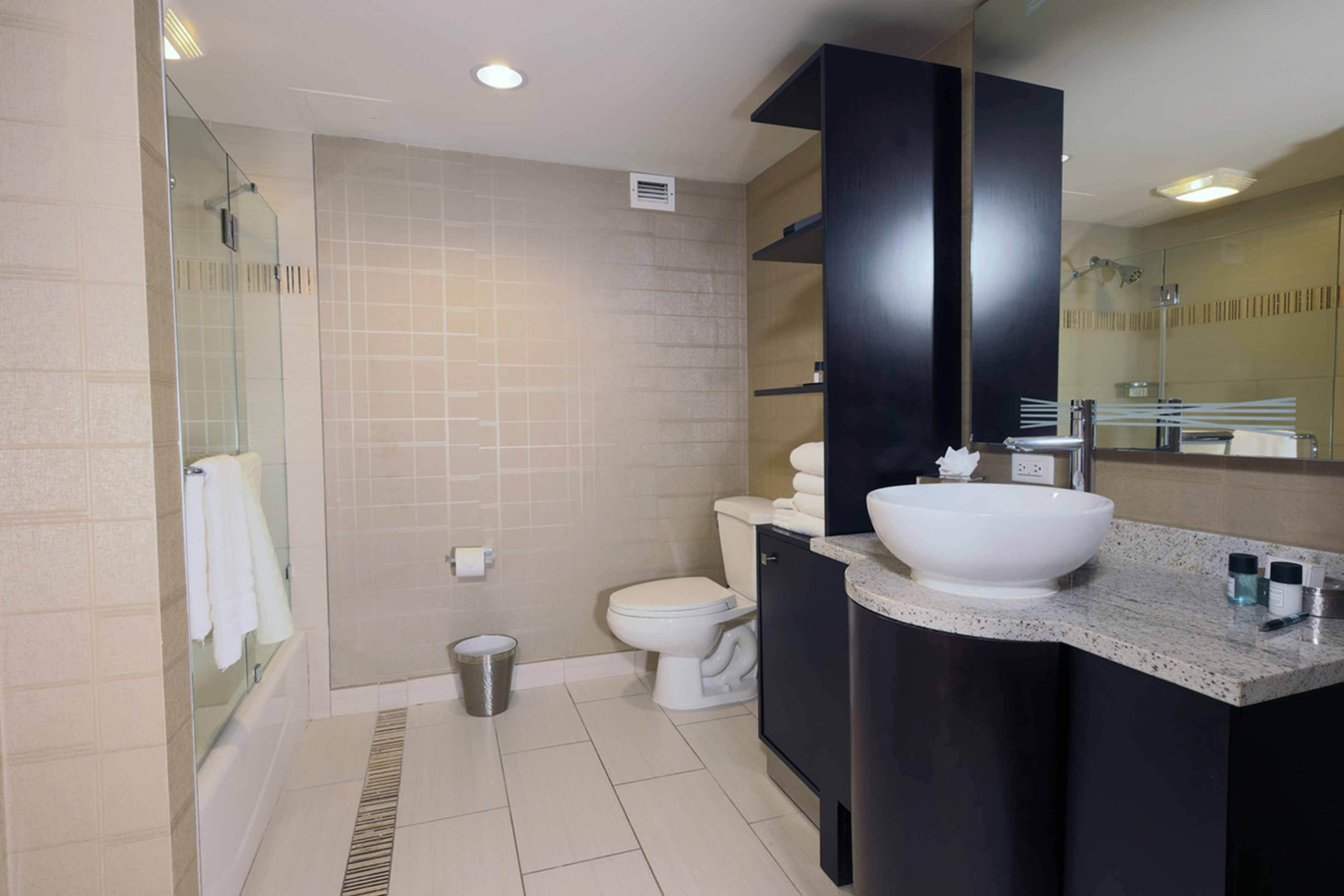 A modern bathroom with a glass-enclosed shower, a white toilet, and a large sink with a dark cabinet.