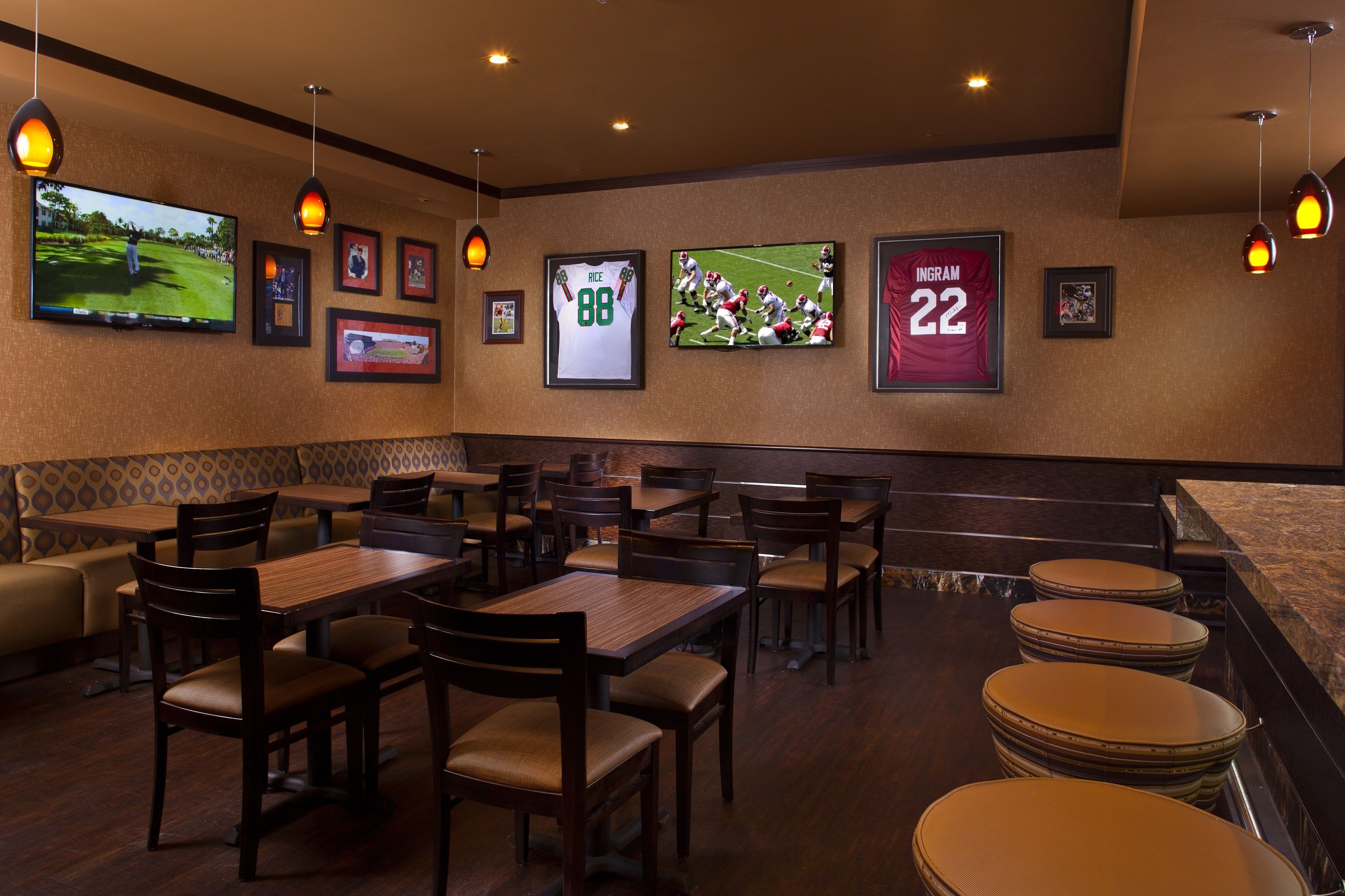 A restaurant with wooden tables and chairs, a TV screen displaying sports, and framed sports jerseys on the wall.