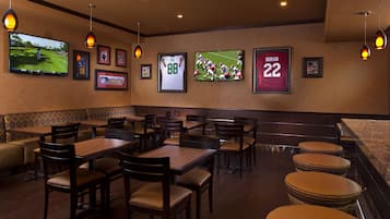 A restaurant with wooden tables and chairs, a TV screen displaying sports, and framed sports jerseys on the wall.