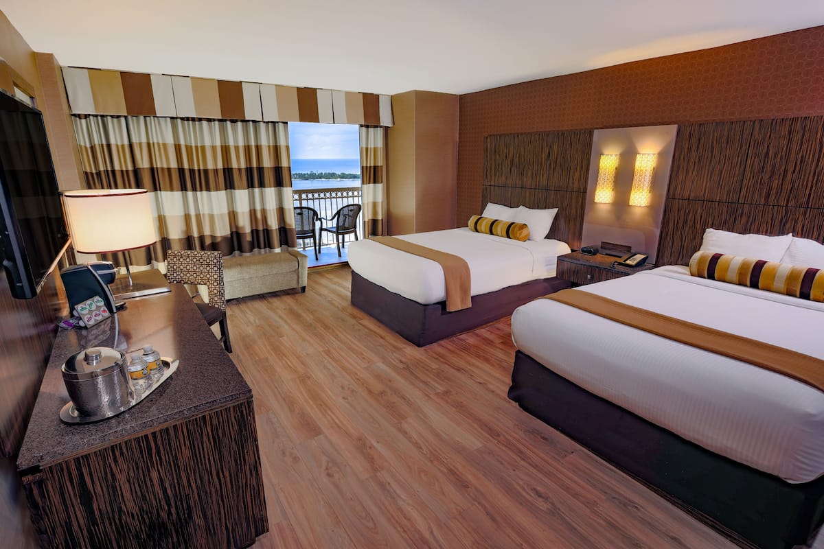 A hotel room with two beds, a desk with a lamp, a chair, and a view of the sea.