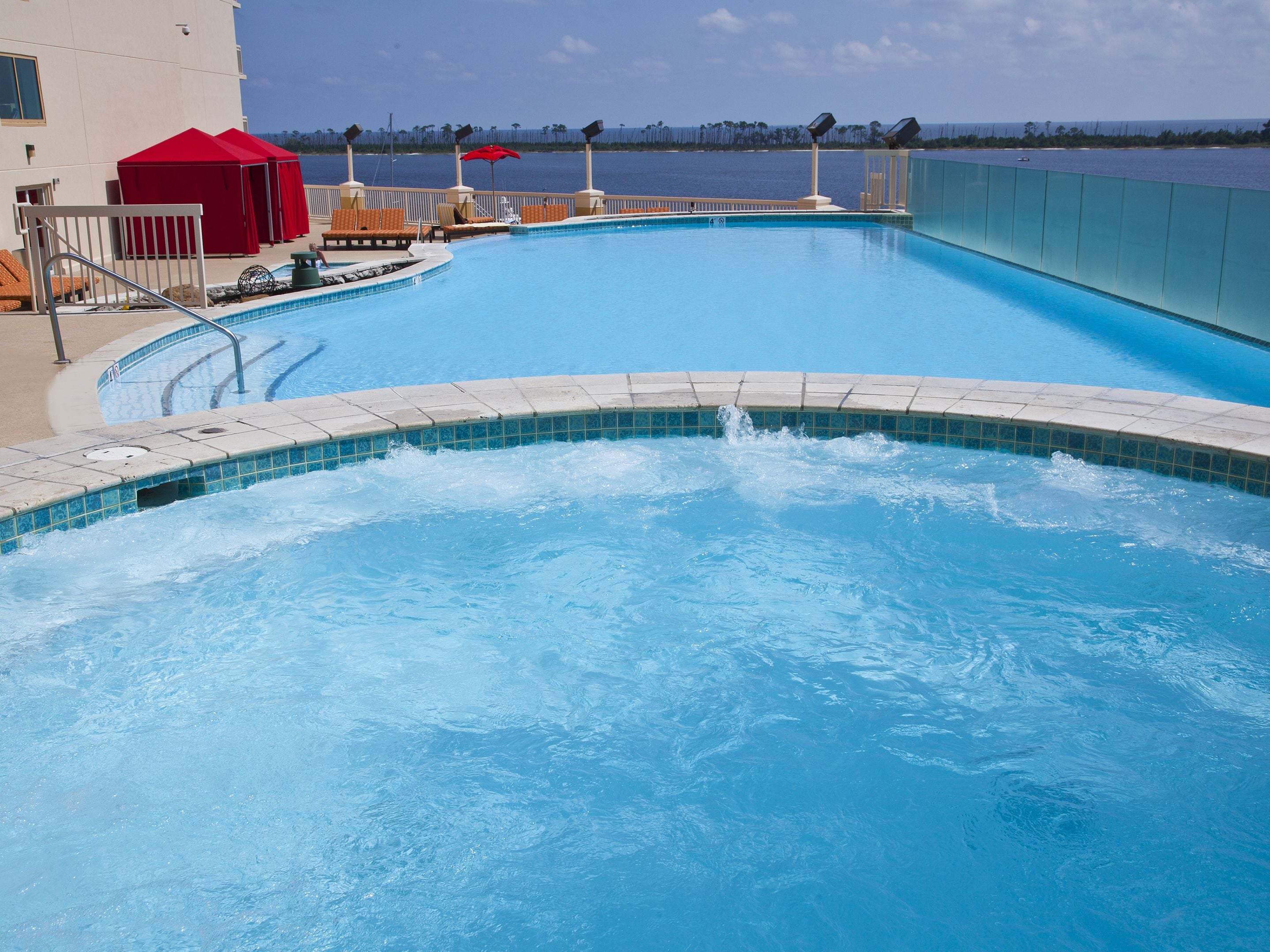 A swimming pool with a view of the ocean, lounge chairs, and a red canopy.